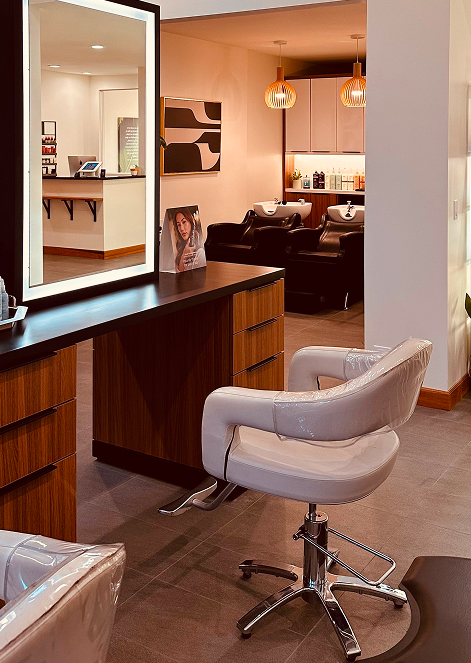 - Indira Salon Spa in Waupaca, WI A modern hair salon interior with a white salon chair, a large mirror, wooden counter, and hair washing stations in the background. - Indira Salon Spa in Waupaca, WI