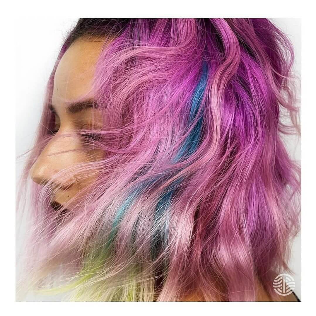 - Indira Salon Spa in Chicago IL, Park Ridge IL, Green Bay WI Person with wavy, shoulder-length hair dyed in shades of pink, purple, blue, and green. The background is plain white. - Indira Salon Spa in Chicago IL, Park Ridge IL, Green Bay WI