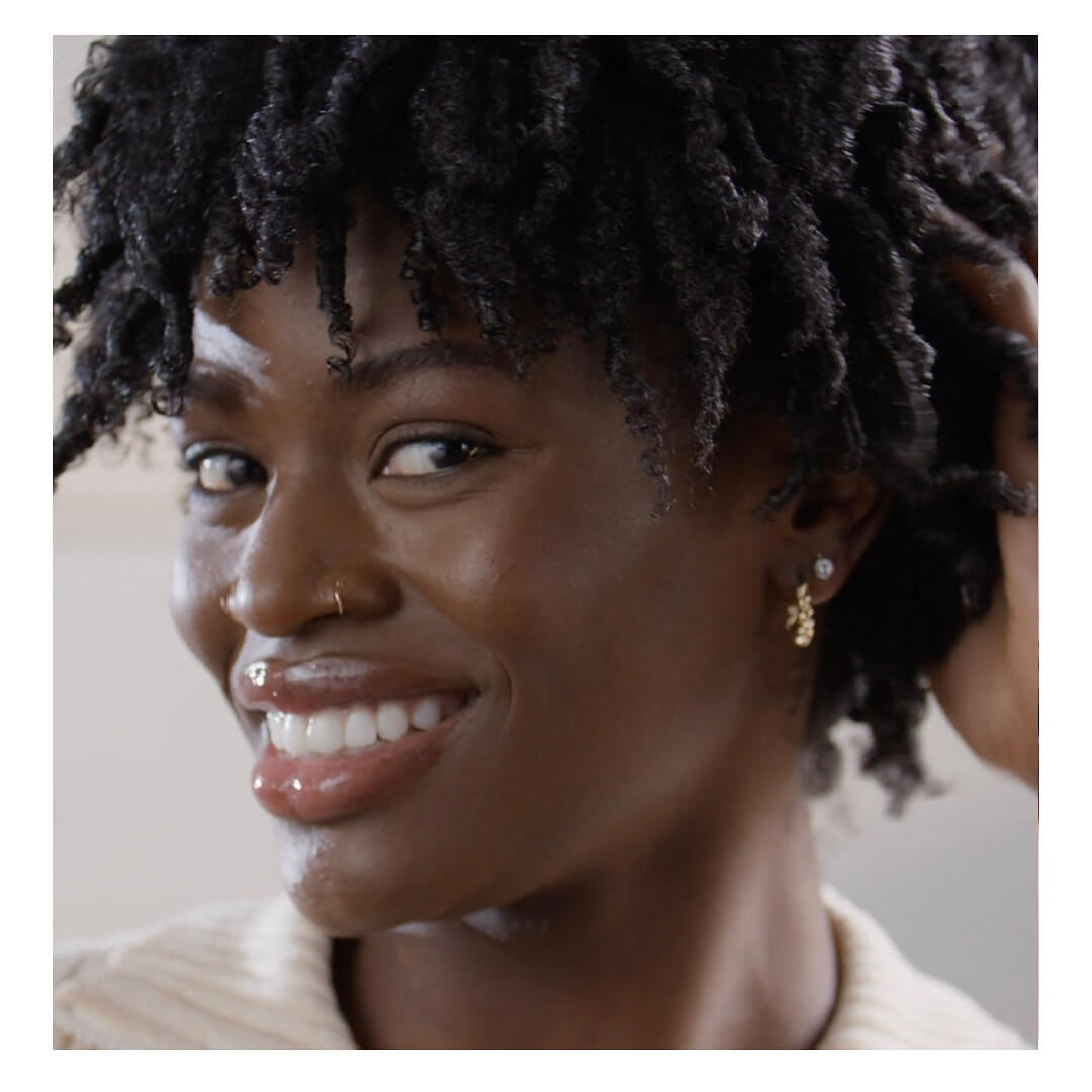 - Indira Salon Spa in Chicago IL, Park Ridge IL, Green Bay WI A person with curly hair smiles at the camera, wearing a nose ring, earrings, and a light-colored top. - Indira Salon Spa in Chicago IL, Park Ridge IL, Green Bay WI