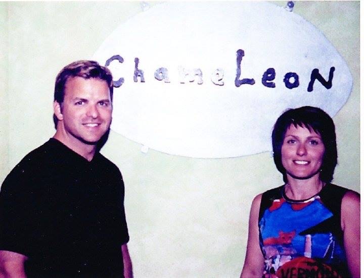 Two people stand in front of a wall sign that reads "Chameleon," showcasing their appreciation for beauty and wellness, much like the experience offered at Indira Salon & Spa. - Indira Salon Spa in Chicago IL, Park Ridge IL, Green Bay WI